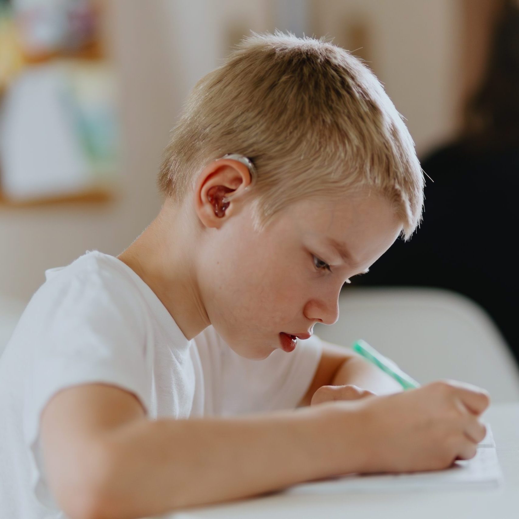 A,Boy,With,Hearing,Aids,Focuses,On,Homework,,Showcasing,Natural